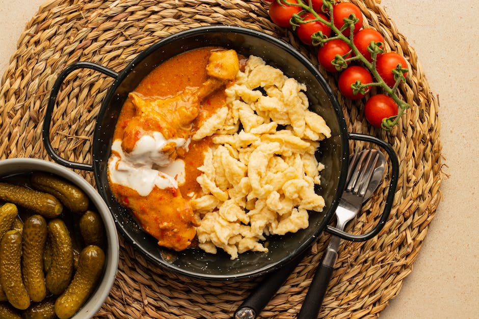 Traditional chicken paprikash with spaetzle, tomatoes, and pickles, served on a woven placemat.