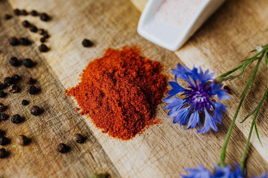 A vibrant display of paprika and peppercorns on a rustic wooden board with a cornflower accent. Perfect for culinary visuals.